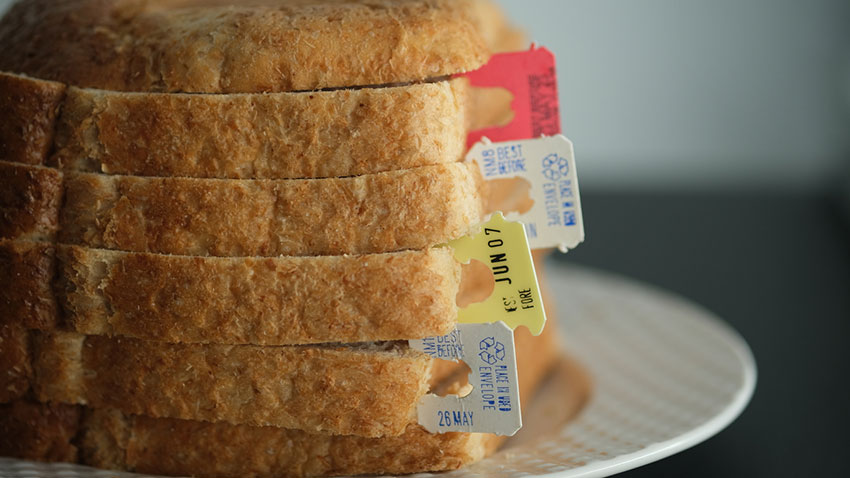 Several slices of white bread are stacked neatly on a plate with several colorful plastic tags with varying expiration dates tucked between the slices.